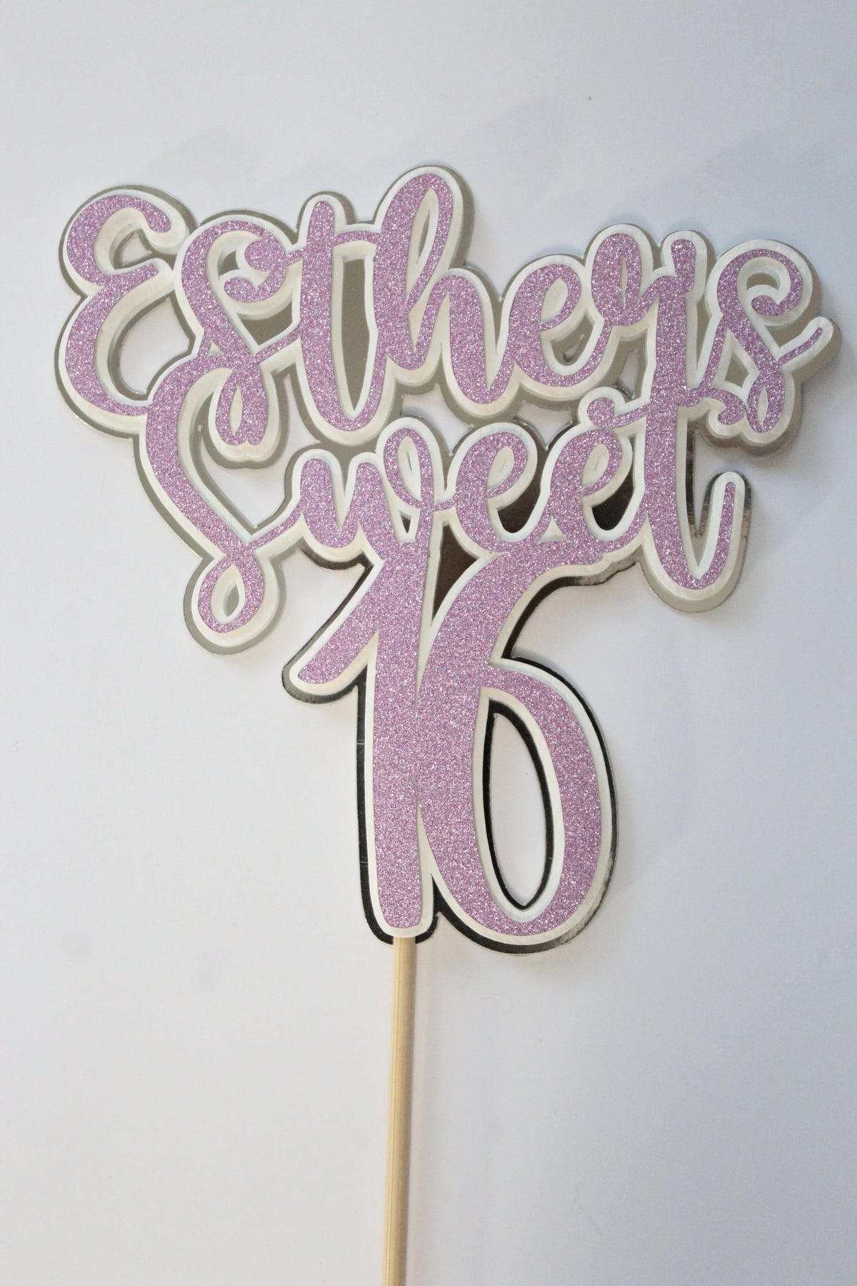 Decorative cake topper with pink glittery design and 'Sweet Sixteen' text on a white background