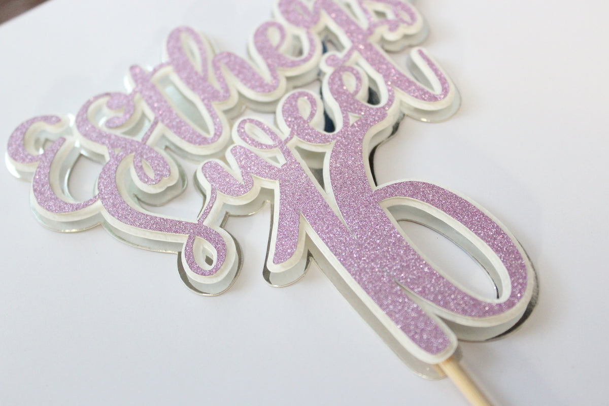 Pink glittery cake topper with 'Esther's 21st' on a white background