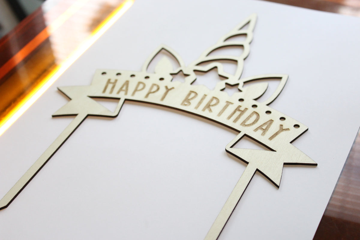 Unicorn themed Wooden birthday cake topper with 'Happy Birthday' text on a white background