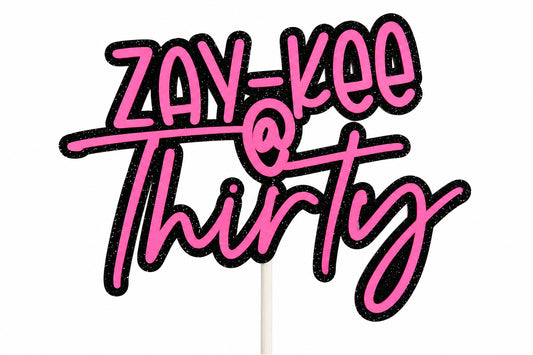 A close-up of a pink and black custom script cake topper reading 'ZAY-KEE @ Thirty' on a white background.